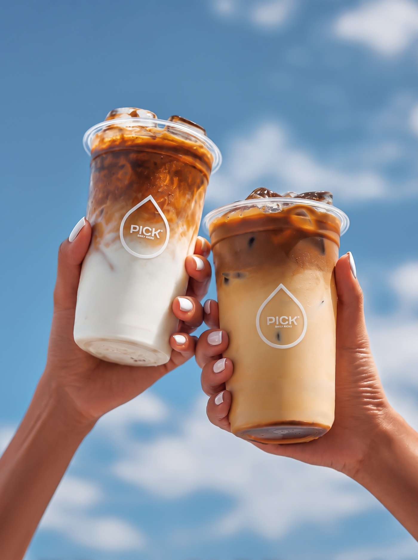Two iced PICK coffees held against a blue sky